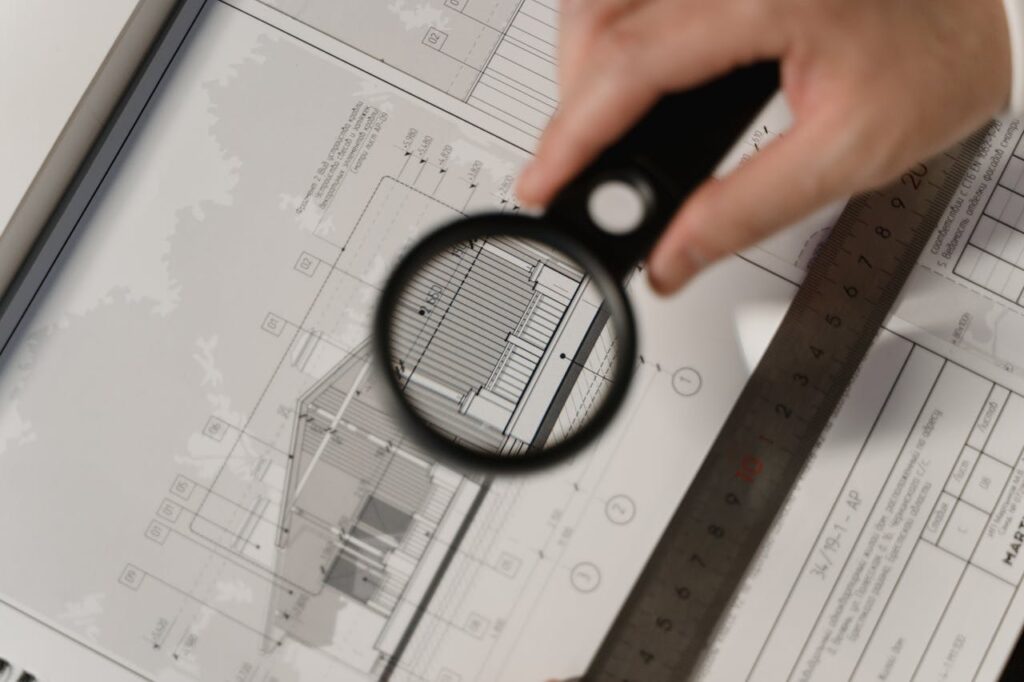 pexels-photo-6615284 Focused view of architectural plans with magnifying glass, ruler, hands.