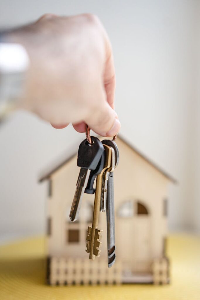 pexels-photo-7599735 Close-up of a hand holding keys with a miniature wooden house in the background, symbolizing real estate investment.
